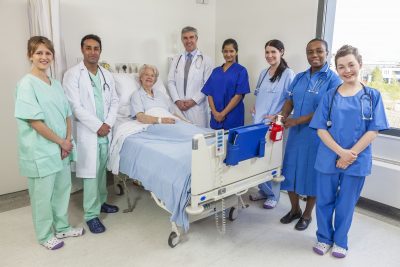 20705719 - senior female woman patient in hospital bed surrounded by the multi ethnic interracial medical team of men and women male and female doctors and nurses